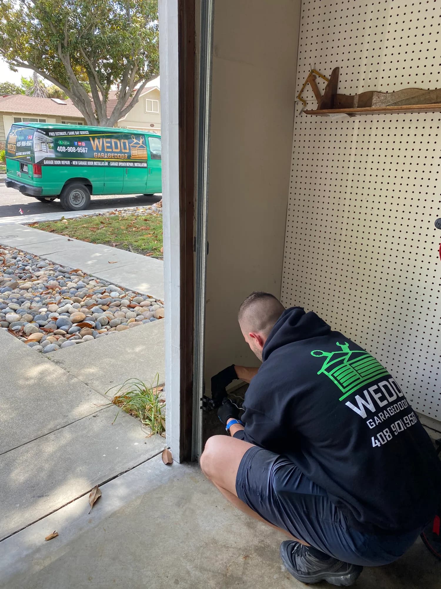 WeDo technician working a residential garage door with the company van parked at the curb